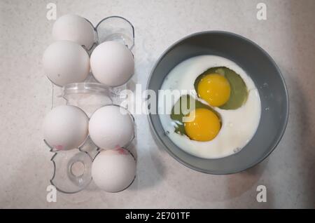 Two raw eggs in a bowl with milk near white eggs in eggshell in egg tray. Food ingredients for cooking omelette for breakfast Stock Photo