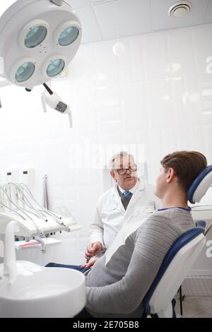 Vertical shot of a senior male dentist having appointment with patient at the clinic Stock Photo