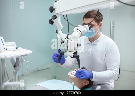 Professional dentist using dental microscope, treating teeth of patient Stock Photo