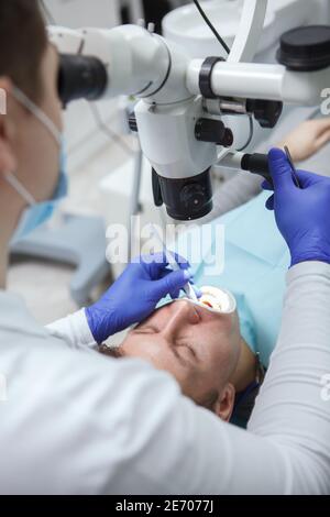 Vertical cropped shot of a male patient having dental treatment by experienced dentist, using microscope Stock Photo
