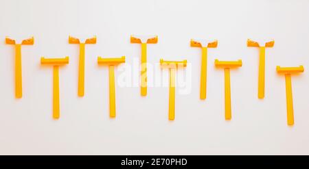 Top view of ten orange yellow shaving plastic simple razors in row at isolated white background,  hygiene, skin care and hair removal concept Stock Photo