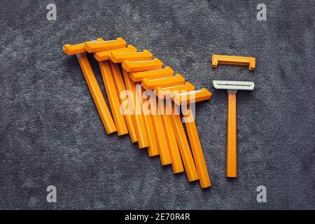 Many plastic disposable cheap shaving orange yellow razors with caps on gray background, hair removal tools set Stock Photo