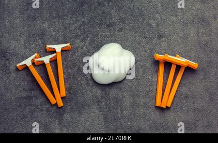 Six disposable orange plastic razors and shaving cream in cloud shape at gray background, grooming and hygiene Stock Photo