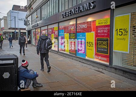 Store closing sign outside the Debenhams shop in Manchester  city centre, with people passing homeless man begging . Stock Photo