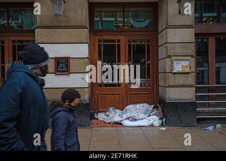 Homeless man sleeps in pub doorway with passing by mother and child  in Manchester . Stock Photo