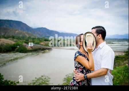 Beautiful couple in love covering faces with a hat and kissing outdoors in nature Stock Photo
