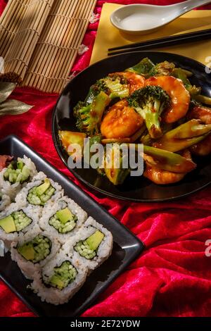 Chinese cuisine szechuan shrimp with vegetables and cucumber avocado sushi roll Stock Photo