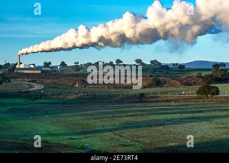Factory in the middle of the field with a chimney that releases a large column of smoke. Stock Photo
