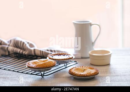 Four mini pies on baking rack with white jug of milk. Breakfast still life Stock Photo