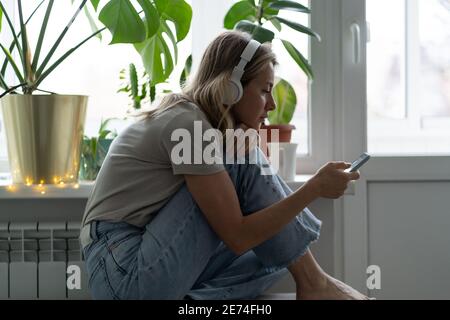 Woman listening to music, wear wireless headphones, using smart phone, chatting in social networks Stock Photo