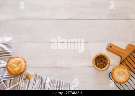 Four mini pies straight from the oven  on white wooden table with milk jug, cutting board Stock Photo