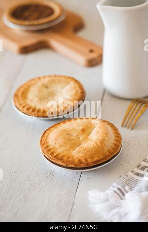 Three mini pies straight from the oven  on white wooden table with milk jug, cutting board Stock Photo