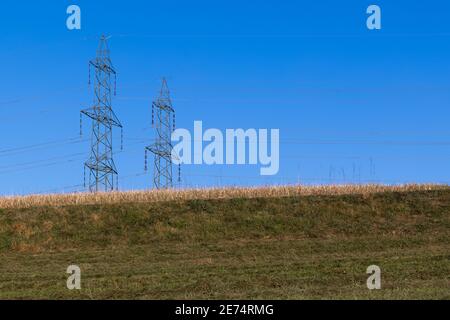 no life without electricity. two big power pylons behind a green hill in a beautiful cloudless blue sky, without people in the daytime Stock Photo