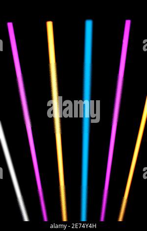 Glowing neon light strips in pink, yellow, blue and white against a black background. Stock Photo