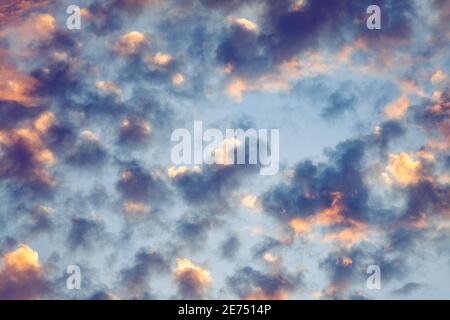 Scattered clouds colored in sunset colors moving across a bright blue sky Stock Photo