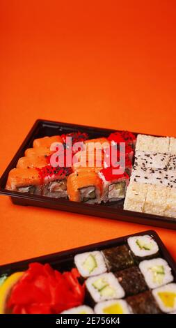 Close up of appetizing sushi in containers on orange background. Set of tasty sushi rolls with different ingredients Stock Photo