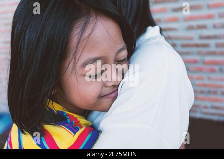 A girl hugs with her mother, the concept of showing love and care at the family home. Stock Photo