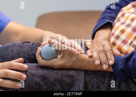 Elderly woman doing rubber ball for exercise fingers, palm ,hand and foot muscle with caregiver take care. Stock Photo