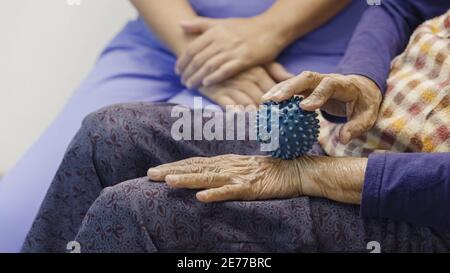 Elderly woman doing rubber ball for exercise fingers, palm ,hand and foot muscle with caregiver take care. Stock Photo