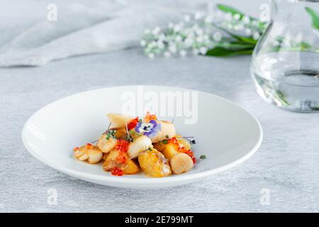 Scallops, potatoes, red caviar, fresh flowers decor in round plate Stock Photo