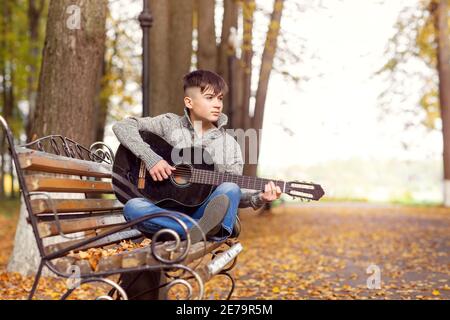 teen boy plays black acoustic guitar on an autumn day in the Park Stock Photo