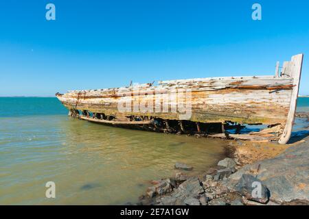 Rotting holed hulk of old wooden fishing boat beached on shore of Ocean Beach Road Southland New Zealand. Stock Photo