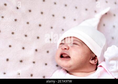 Childhood, illness, colic, bloating, motherhood, health concepts - Close up restless, worried sad newborn baby girl in hat sleeps crying scream have Stock Photo