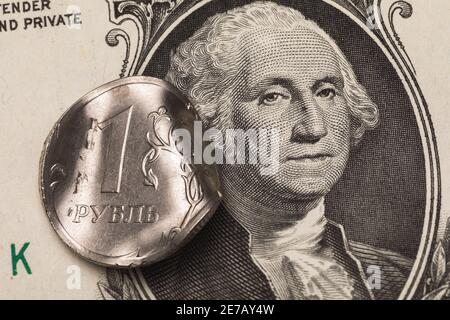 Deformed coin one ruble on the background of the dollar banknote, close-up. On the coin the inscription in Russian letters ruble. Stock Photo