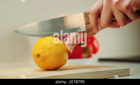 Close-up shot of hands with knife cutting lemon on the kitchen board. Stock Photo