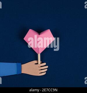 Hand holding Origami Heart. Valentine's Day card, paper cutting. Flat lay, copy space. Valentine Day Paper Art. Holiday, birthday, valentine concept. Stock Photo