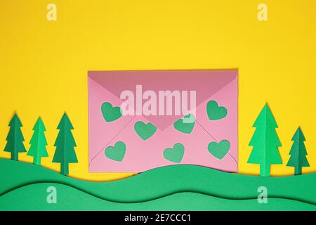 Festive card. Paper green hearts and pink envelope on yellow background. Creative paper cut background with paper envelope. Paper art on valentine day Stock Photo