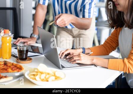 Happy business team workers talking about project and sharing meal enjoying having fun at work Having Meeting Eating Pizza and potato chips. Stock Photo