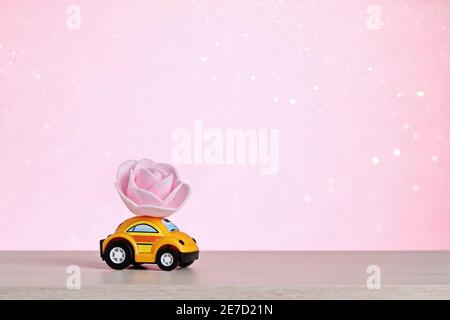 A yellow car carries a rose flower. Happy Valentine's Day, February 14th. Flower delivery. Valentine's Day card. March 8, international women's day, mother's day. Stock Photo