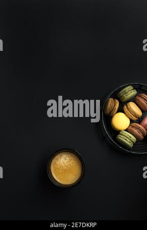 Overhead view of a foamy coffee next to a metal circled tray full of french macaroons. Stock Photo