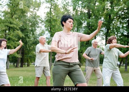 Group of mature people doing exercises with trainer in the park outdoors Stock Photo