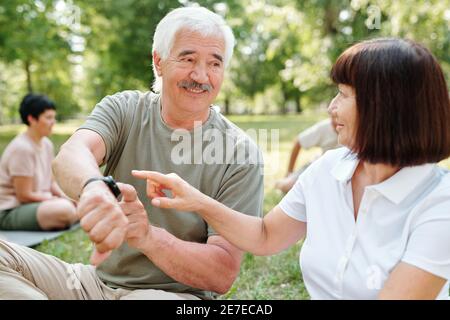 Mature man showing the time on his watch and talking to mature woman while they sitting in the park Stock Photo