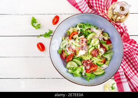 Ketogenic salad with prosciutto, tomatoes, cucumber, lettuce, red onion  and cheese  in  bowl.  Concept healthy appetizer. Keto, paleo food. Top view, Stock Photo