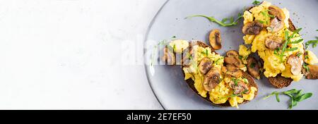 Scrambled eggs and fried mushrooms on bread. Homemade breakfast or brunch meal - scrambled eggs and mushrooms sandwiches. Top view, banner, copy space Stock Photo