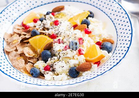 Bowl of flakes with cottage cheese and yogurt, blueberryes and pomegranate on white table. Fitness food. Stock Photo