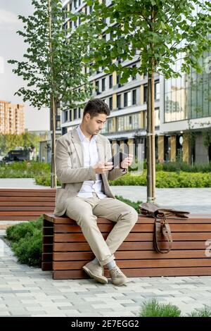 Young businessman using digital tablet in his work while sitting on the bench in the city Stock Photo