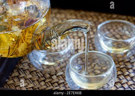 Herbal tea of drying flowers is pouring to cup, close up. A teapot and cup with flowers tea on table. Stock Photo