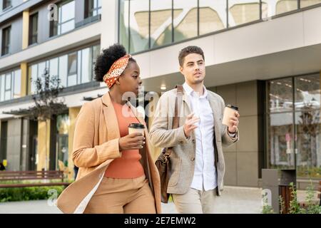Multiethnic couple talking to each other and drinking coffee while walking in the city Stock Photo