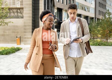 Young businessman using digital tablet and talking to his colleague during their walk in the city Stock Photo
