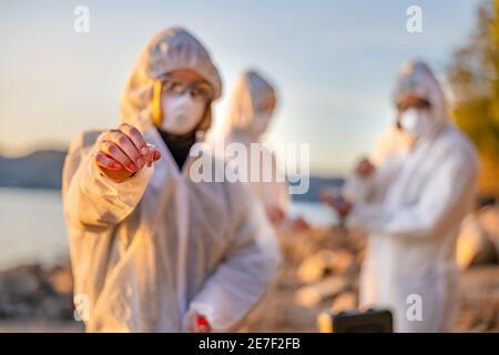 Scientist in white protective suit holding water sample at beach Stock Photo