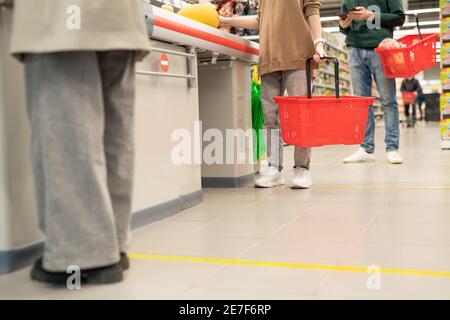 Low section of several customers with plastic shopping baskets standing in queue by checkout counter in large contemporary supermarket Stock Photo