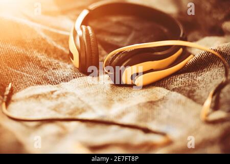 Yellow large headphones with a microphone lie on the bed, illuminated by bright warm sunlight. Music and inspiration. A pleasant pastime. Stock Photo
