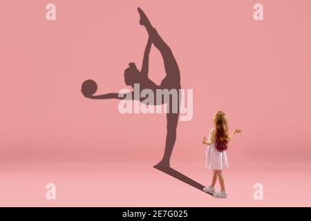 Childhood and dream about big and famous future. Conceptual image with girl and drawned shadow of female rhythm gymnast on coral pink background. Childhood, dreams, imagination, education concept. Stock Photo