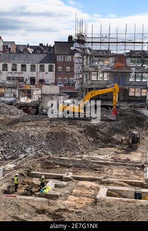 Demolition site (rubble, machinery, excavator demolishing, digger, building shell, archaeologists working in trench) - Hudson House, York, England UK. Stock Photo