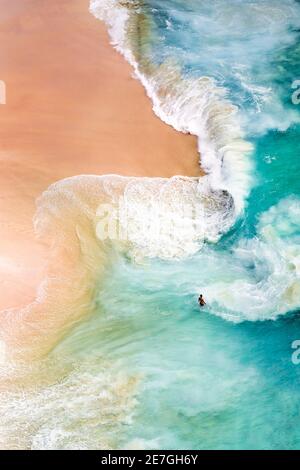View from above, stunning aerial view of a person relaxing on a beautiful beach bathed by a turquoise sea during sunset. Kelingking beach, Nusa Penida Stock Photo