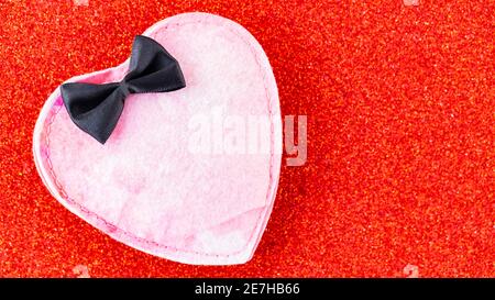 Pink felt heart on a red glitter background. Felt heart with black bow tie. Valentine's Day concept. Copy space. Top view Stock Photo